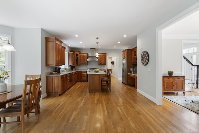 kitchen featuring brown cabinets, ventilation hood, light wood finished floors, a center island, and appliances with stainless steel finishes