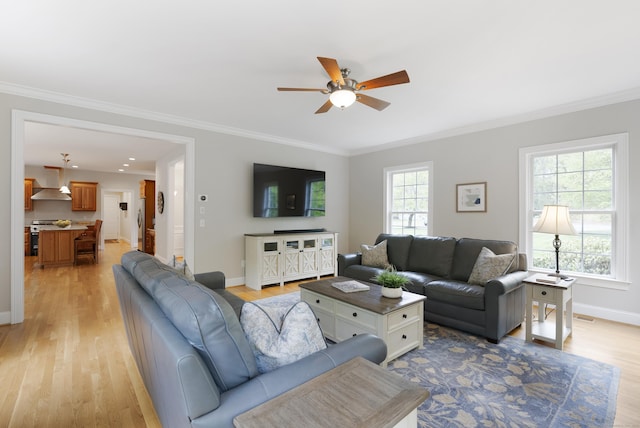 living room featuring ceiling fan, ornamental molding, baseboards, and light wood-type flooring