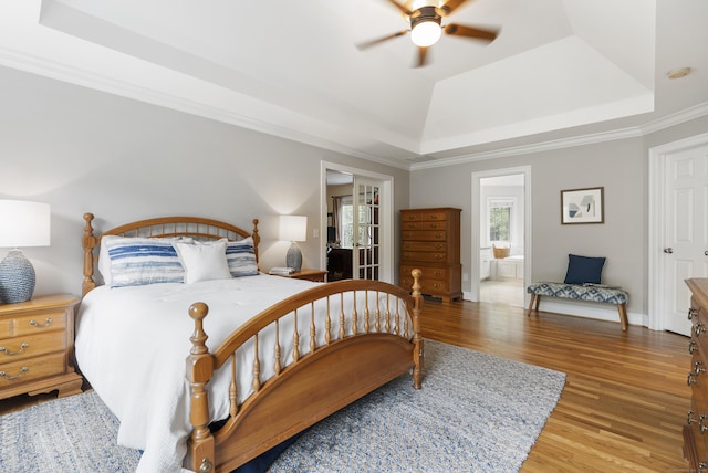bedroom featuring a tray ceiling, light wood-type flooring, baseboards, and a ceiling fan