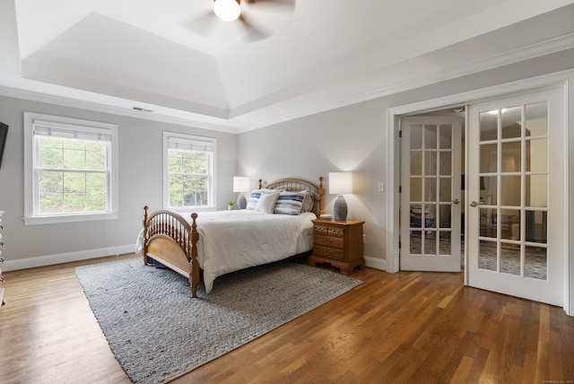 bedroom featuring wood finished floors, french doors, visible vents, baseboards, and a raised ceiling