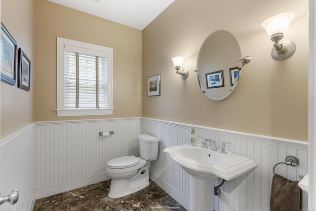 bathroom featuring toilet, a sink, and a wainscoted wall