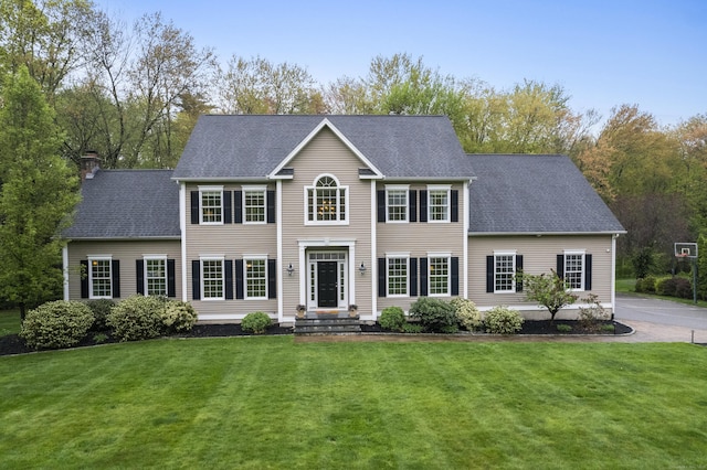 colonial house featuring a shingled roof, a chimney, and a front yard