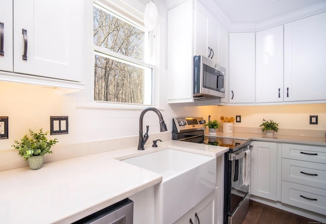 kitchen with white cabinets, stainless steel appliances, a sink, and light countertops