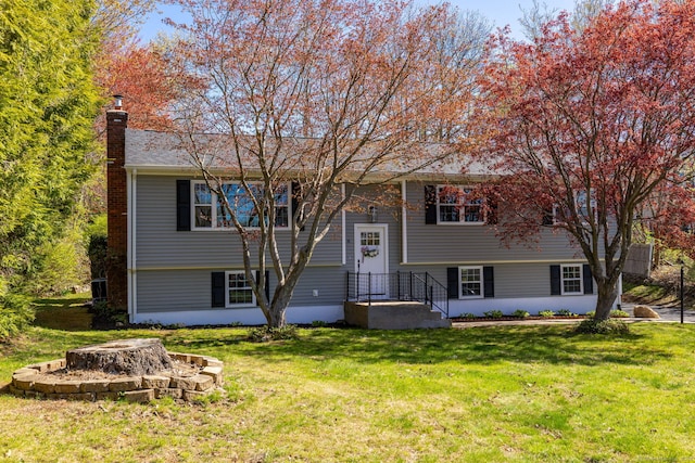raised ranch with an outdoor fire pit, a chimney, and a front lawn
