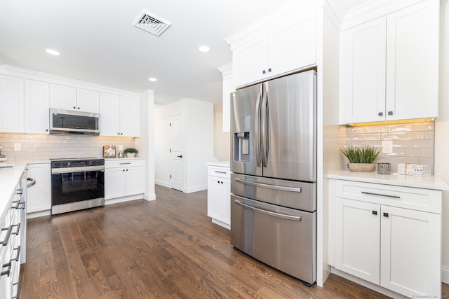 kitchen featuring visible vents, dark wood-style flooring, white cabinetry, backsplash, and stainless steel appliances