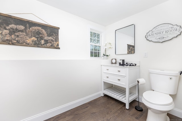 half bathroom with baseboards, wood finished floors, toilet, and vanity
