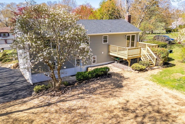 back of house featuring a wooden deck, roof with shingles, and a chimney