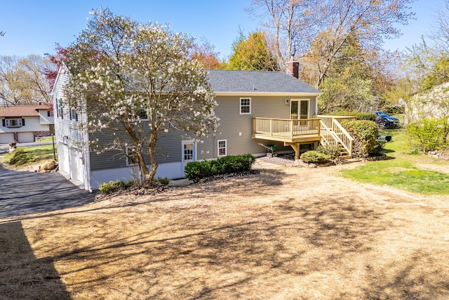 back of property with a garage, a deck, a chimney, driveway, and stairway