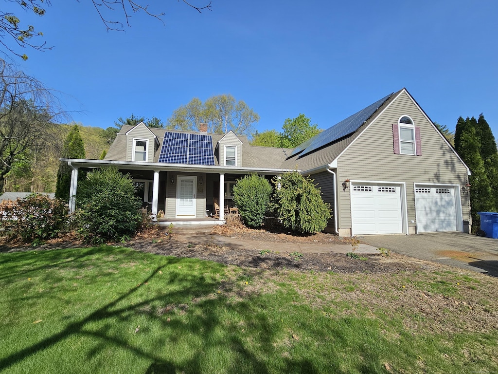 view of front of home featuring roof mounted solar panels, covered porch, a chimney, and a front lawn