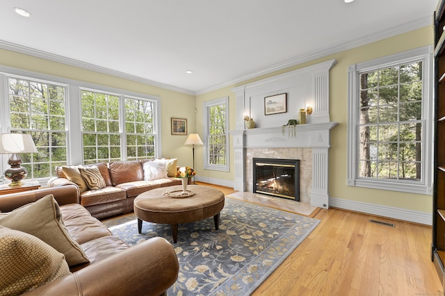 living area featuring visible vents, baseboards, light wood finished floors, ornamental molding, and a premium fireplace