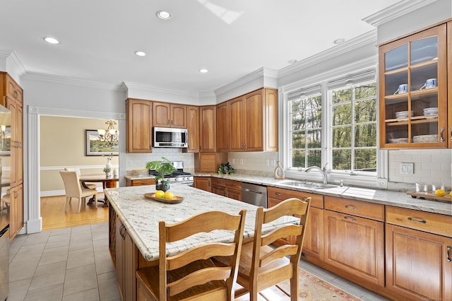 kitchen with brown cabinetry, light stone countertops, tasteful backsplash, a sink, and appliances with stainless steel finishes