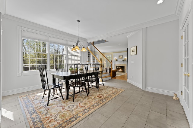 dining space featuring crown molding, an inviting chandelier, a glass covered fireplace, baseboards, and light tile patterned floors