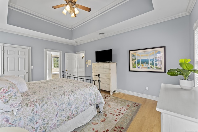 bedroom with a raised ceiling, baseboards, ornamental molding, and light wood finished floors