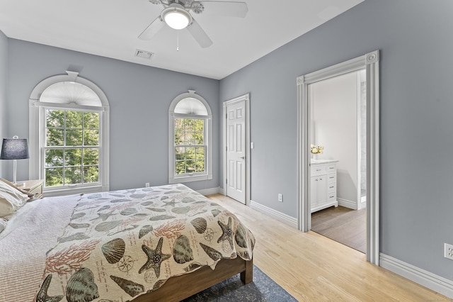 bedroom featuring ceiling fan, visible vents, light wood-type flooring, baseboards, and ensuite bath