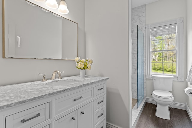 full bath with vanity, wood finished floors, toilet, baseboards, and tiled shower
