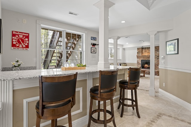 bar with decorative columns, a brick fireplace, and a wealth of natural light