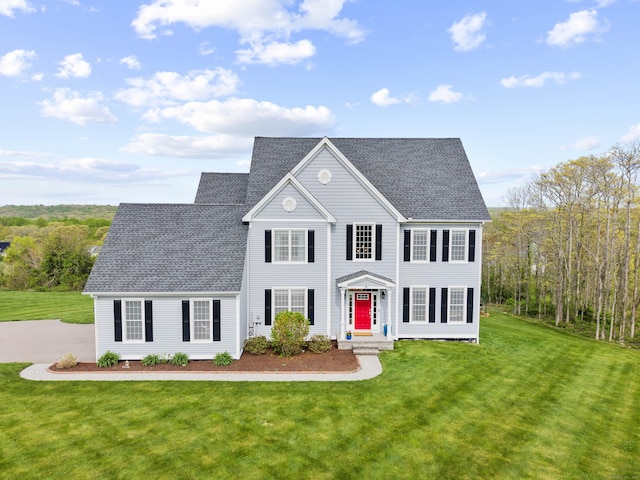 colonial house featuring a shingled roof and a front lawn