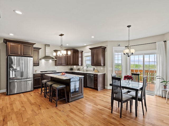 kitchen with dark brown cabinetry, an inviting chandelier, stainless steel appliances, and wall chimney range hood