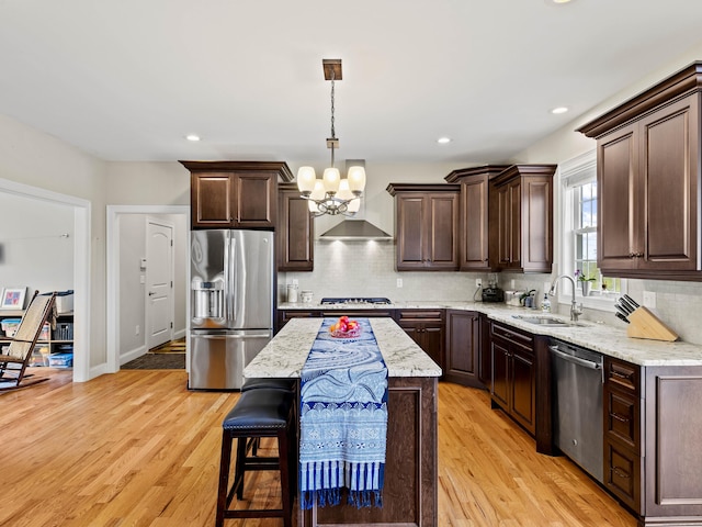 kitchen featuring a sink, stainless steel appliances, wall chimney exhaust hood, dark brown cabinetry, and a chandelier