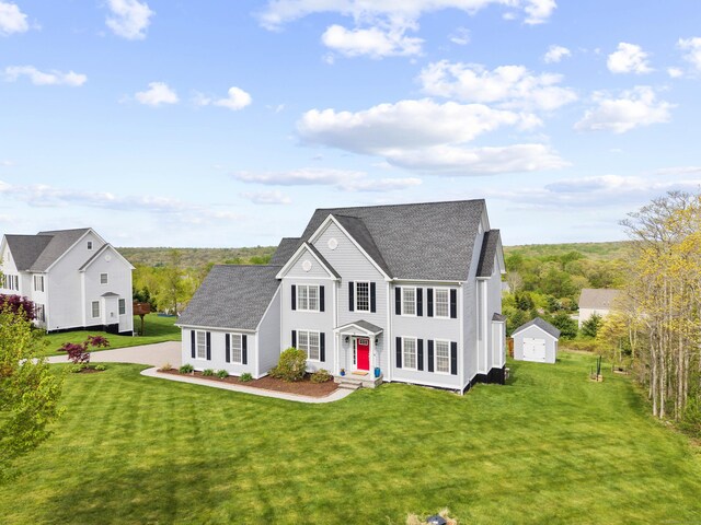 view of front of house featuring a storage shed, an outdoor structure, a front yard, and a shingled roof