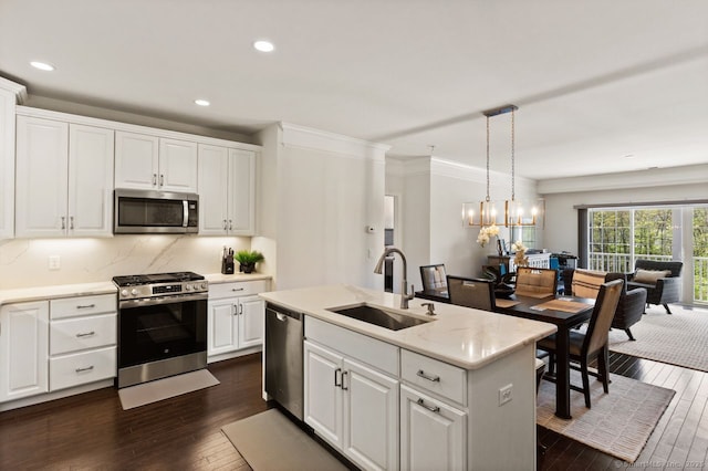 kitchen featuring appliances with stainless steel finishes, hanging light fixtures, a sink, white cabinets, and dark wood-type flooring