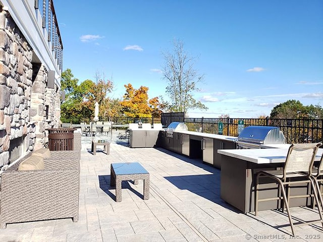view of patio with grilling area, exterior kitchen, fence, and outdoor wet bar