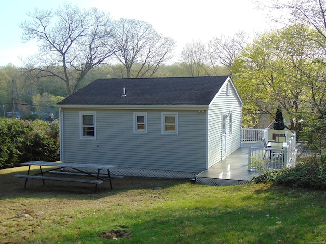 back of property featuring a lawn, a deck, and roof with shingles