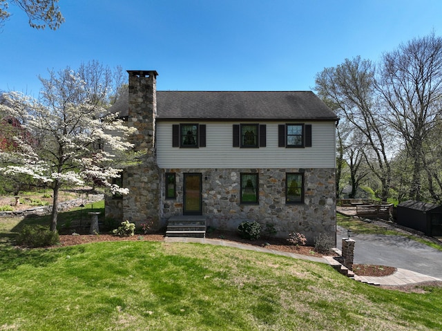 view of front facade with a front lawn, stone siding, and a chimney