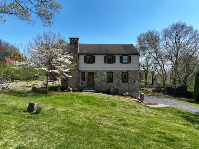 colonial house with a chimney, a front yard, and stone siding