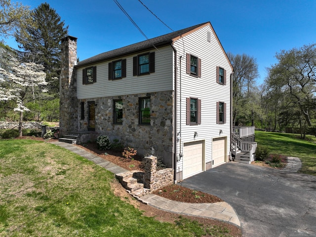 view of front of house with stone siding, a garage, a front yard, a chimney, and driveway