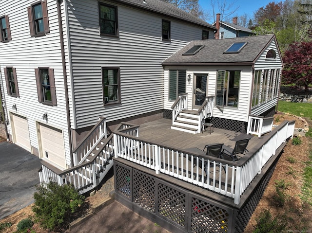 rear view of property with roof with shingles, an attached garage, aphalt driveway, a wooden deck, and a sunroom