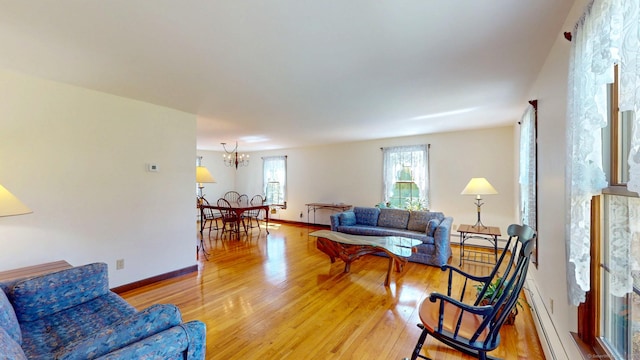 living room with baseboards, light wood finished floors, a baseboard heating unit, and a chandelier