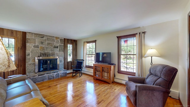 living area featuring a baseboard heating unit, a stone fireplace, baseboard heating, and wood finished floors
