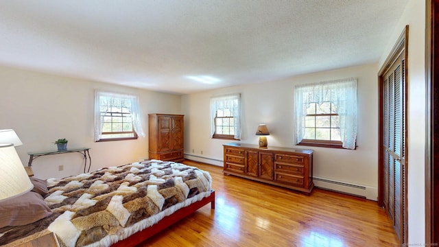 bedroom with multiple windows, baseboard heating, and light wood-style flooring