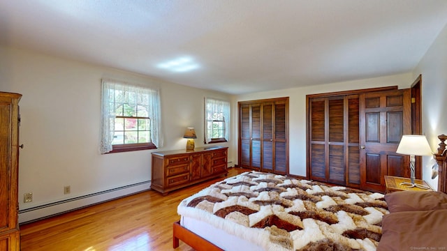 bedroom with multiple closets, a baseboard heating unit, and light wood-style floors