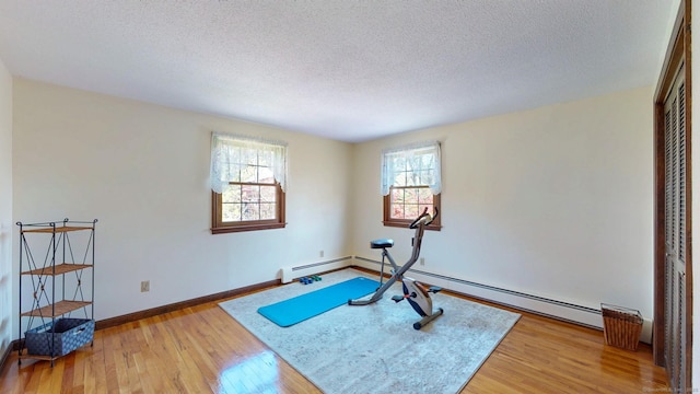 workout room with a textured ceiling, a baseboard radiator, baseboards, and light wood-style floors