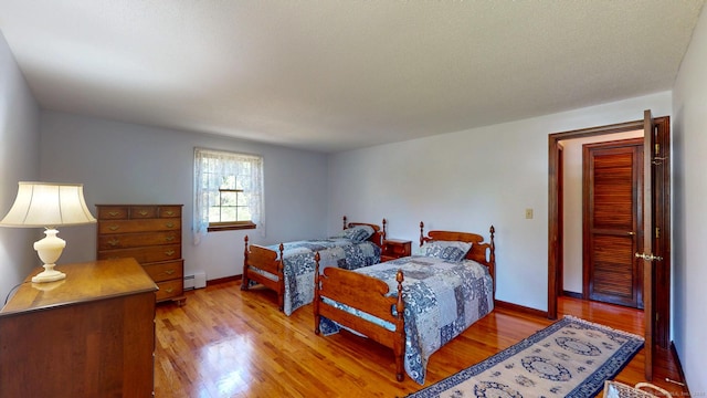 bedroom with light wood-style floors, baseboards, and a baseboard heating unit