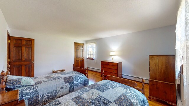 bedroom featuring wood finished floors and a baseboard heating unit