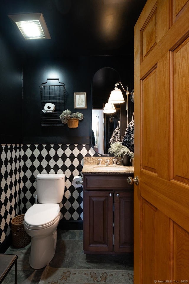 130 Upper Whittemore Rd, Middlebury, CT 06762 - bathroom with vanity, toilet, tile walls, stone finish floor, and a wainscoted wall