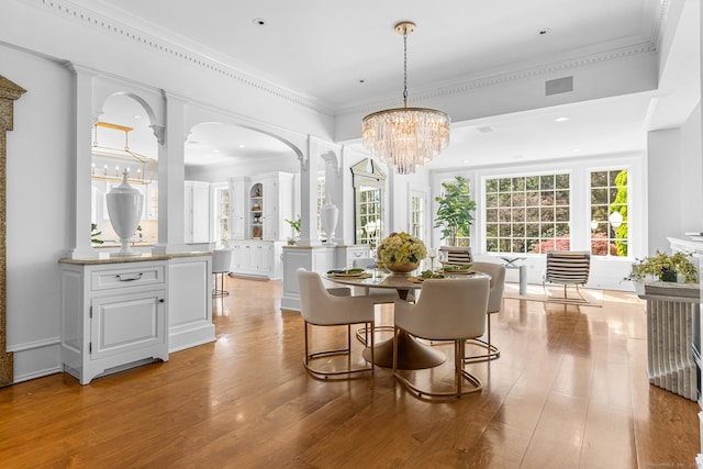 dining room featuring light wood-style floors, arched walkways, a chandelier, visible vents, and ornamental molding