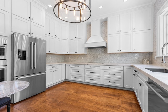 kitchen featuring appliances with stainless steel finishes, wood finished floors, a sink, custom exhaust hood, and white cabinetry