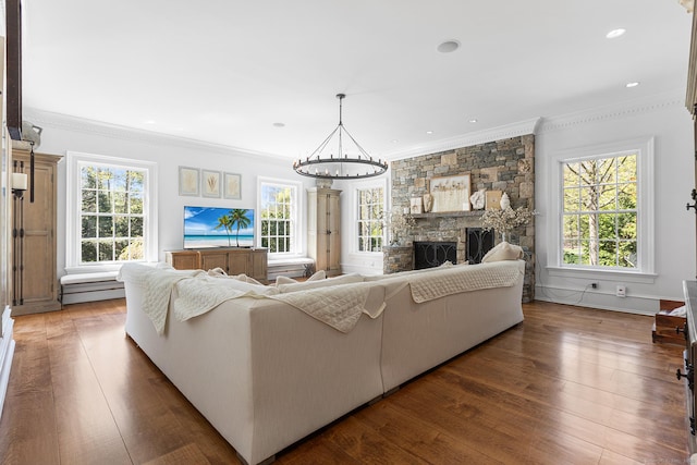 living room with crown molding, a stone fireplace, hardwood / wood-style floors, and a chandelier