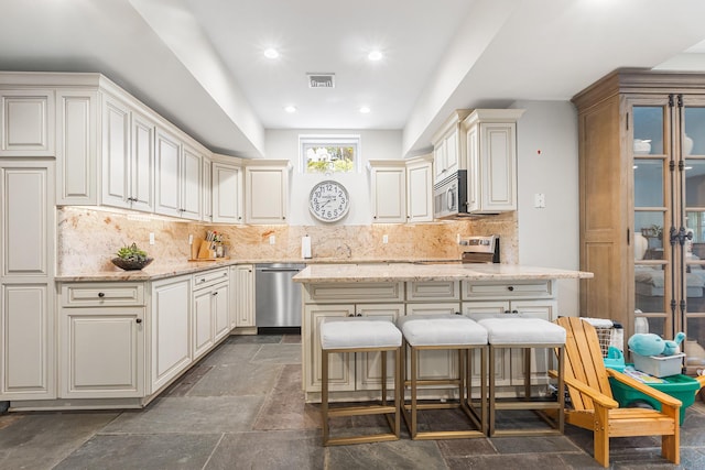 kitchen featuring visible vents, decorative backsplash, stone tile flooring, light stone counters, and stainless steel appliances