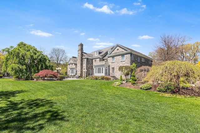 view of front of property featuring a front yard, a chimney, and stone siding