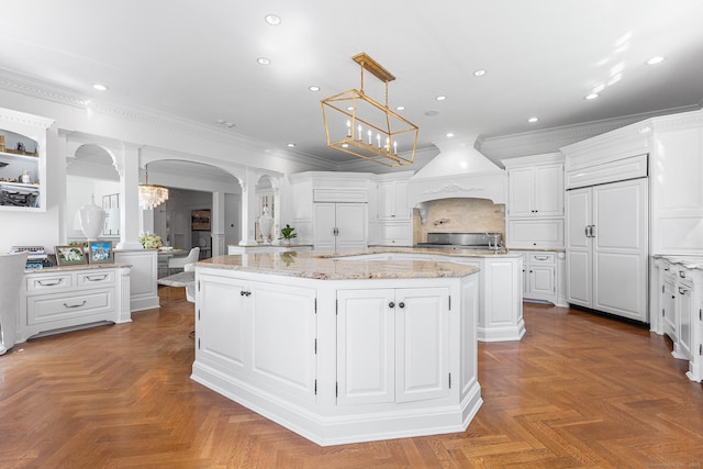 2959 Congress St, Fairfield, CT 06824 - kitchen featuring arched walkways, a center island with sink, white cabinets, ornamental molding, and ornate columns
