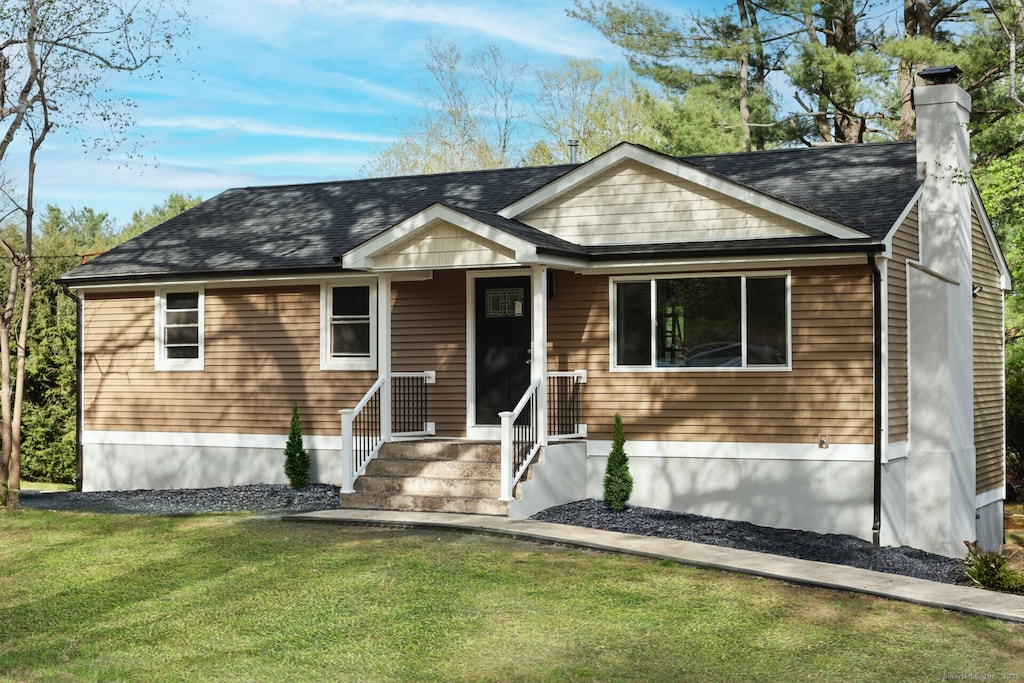 view of front of house featuring a shingled roof, a chimney, and a front lawn