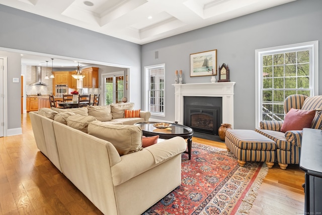 living area with coffered ceiling, light wood-style flooring, a glass covered fireplace, beamed ceiling, and recessed lighting