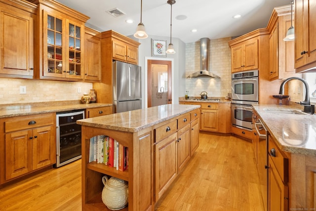 kitchen with stainless steel appliances, wall chimney range hood, beverage cooler, a sink, and backsplash