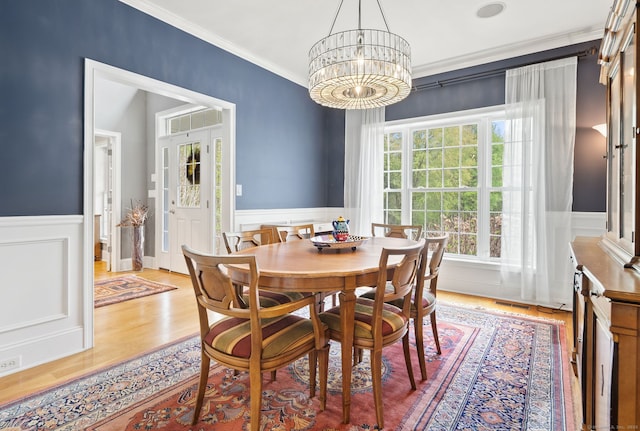 dining room with ornamental molding, a wainscoted wall, a decorative wall, light wood finished floors, and a chandelier