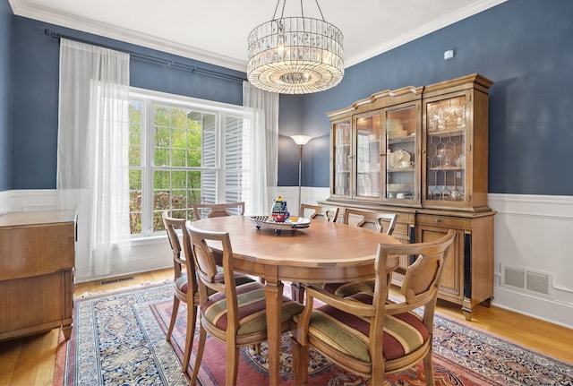 dining space featuring a chandelier, wainscoting, crown molding, and light wood finished floors